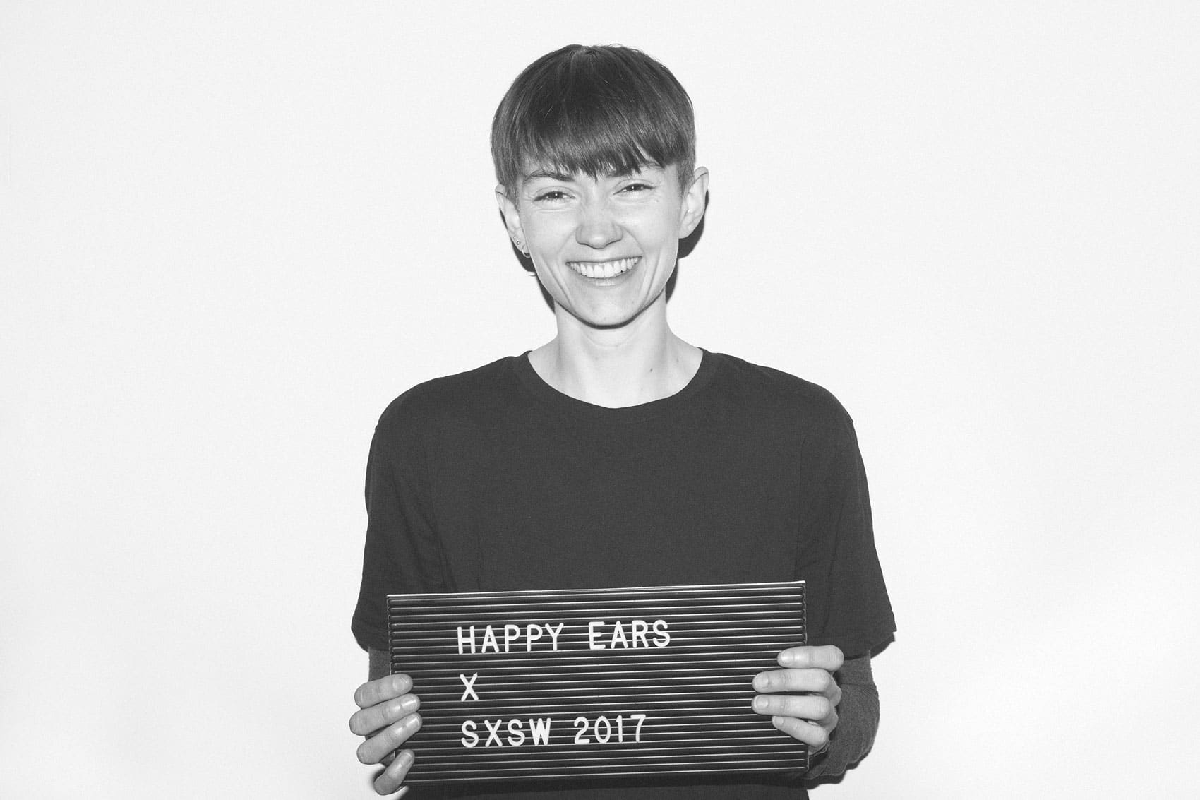 smiling woman with short hair holding up Happy Ears sign